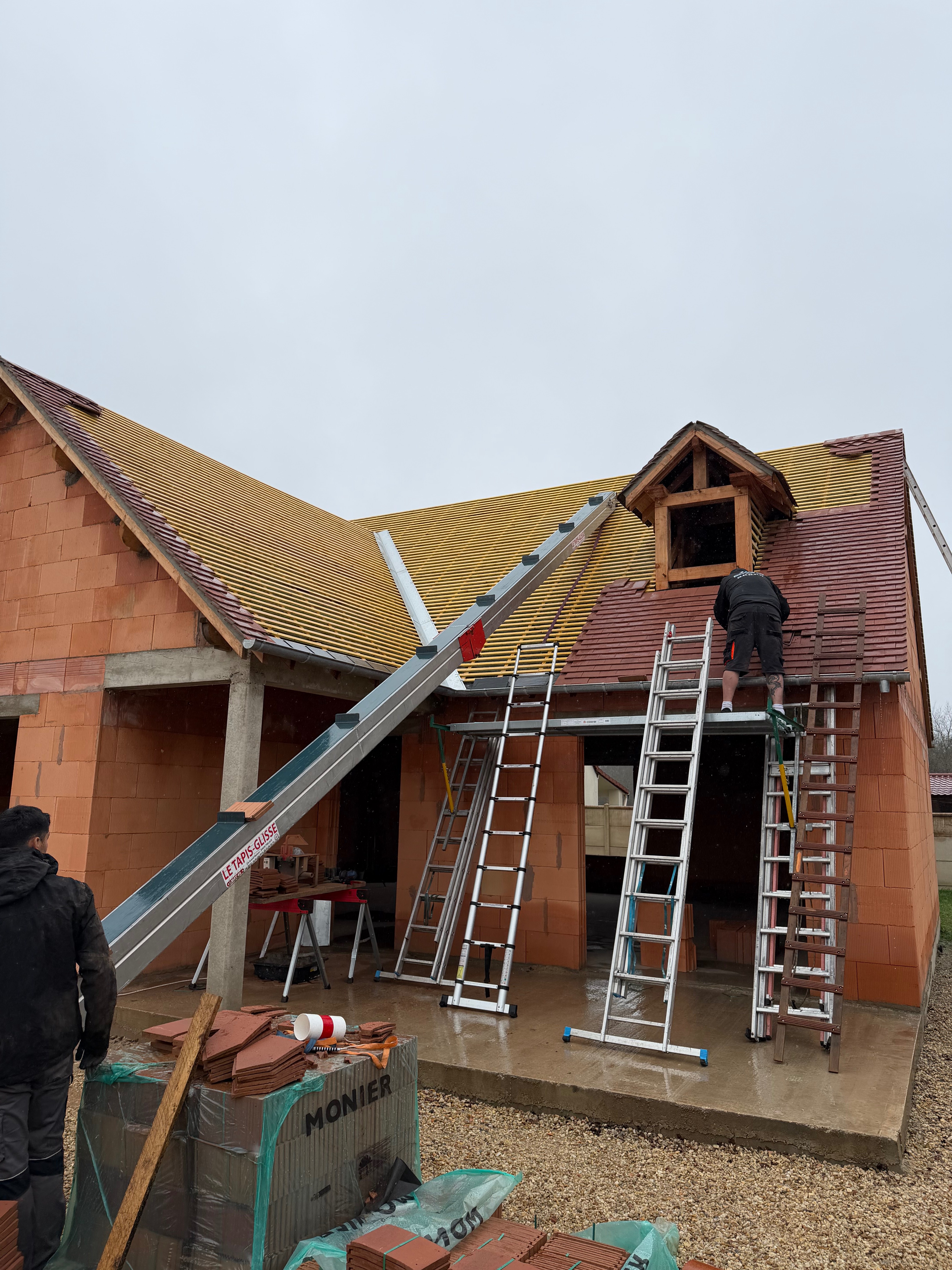 Pose de tuiles plates en terre cuite sur une maison neuve, avec monte-matériaux et échelles